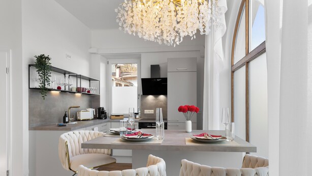 A modern kitchen with a central island, white chairs, and a chandelier.