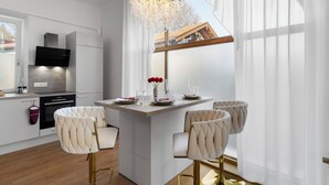 A modern kitchen with a central island, white cabinetry, and a large window with sheer curtains.