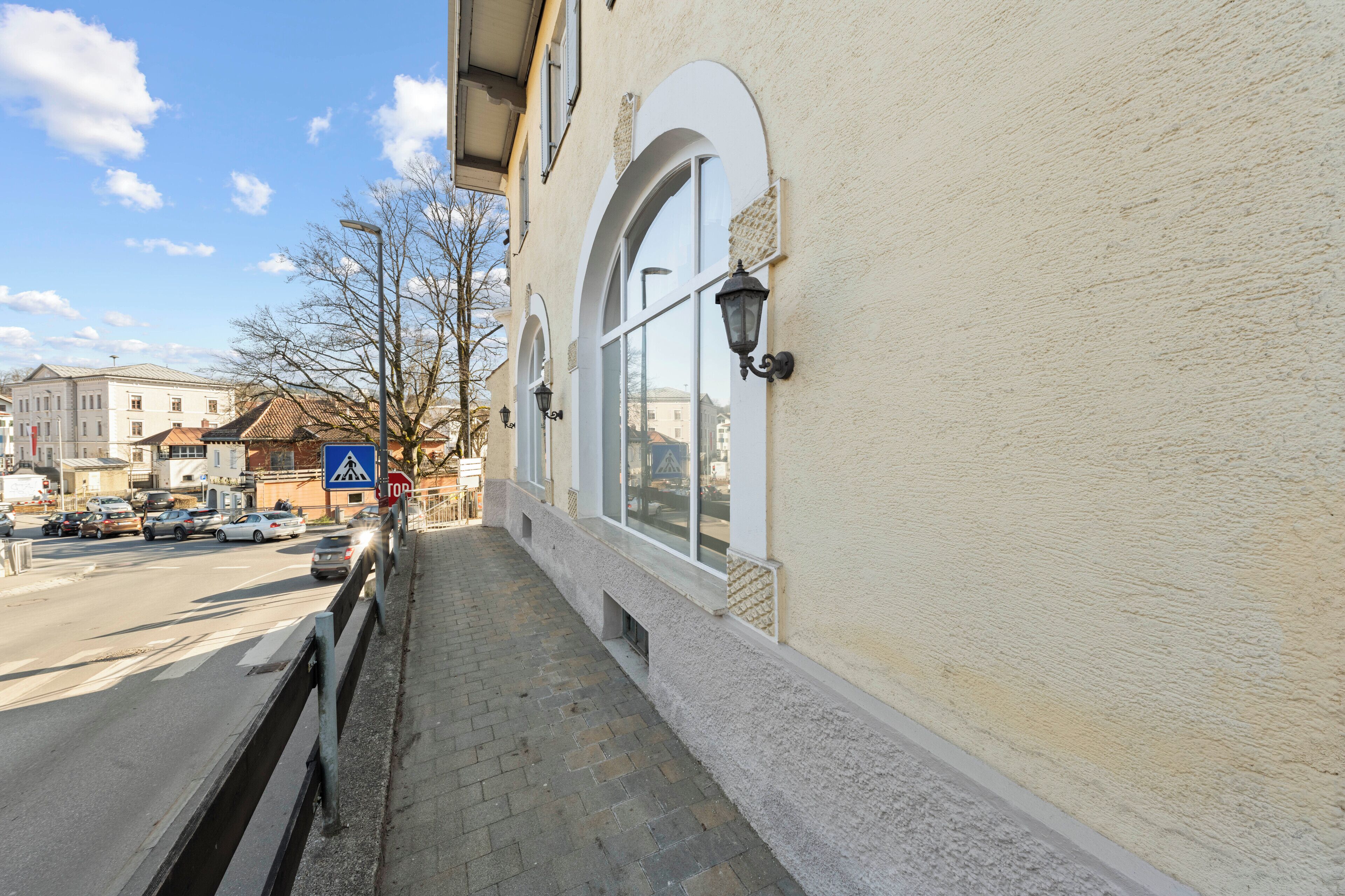 A sidewalk next to a building with large windows and a street view.