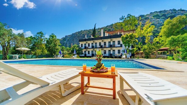 A poolside area with lounge chairs, a table with fruit and drinks, and a building with balconies in the background. - Patara Gate Boutique Hotel (Kas)