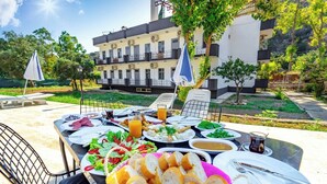 An outdoor dining area with a variety of dishes, including bread, salads, and beverages, set against a backdrop of a building with balconies and trees. - Patara Gate Boutique Hotel (Kas)