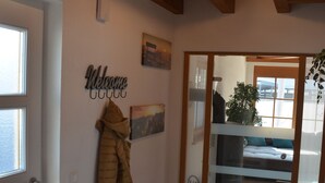 Ein Flur mit Kleiderständer, einer Willkommensanzeige und Blick in einen Raum mit Bett und Fenster.