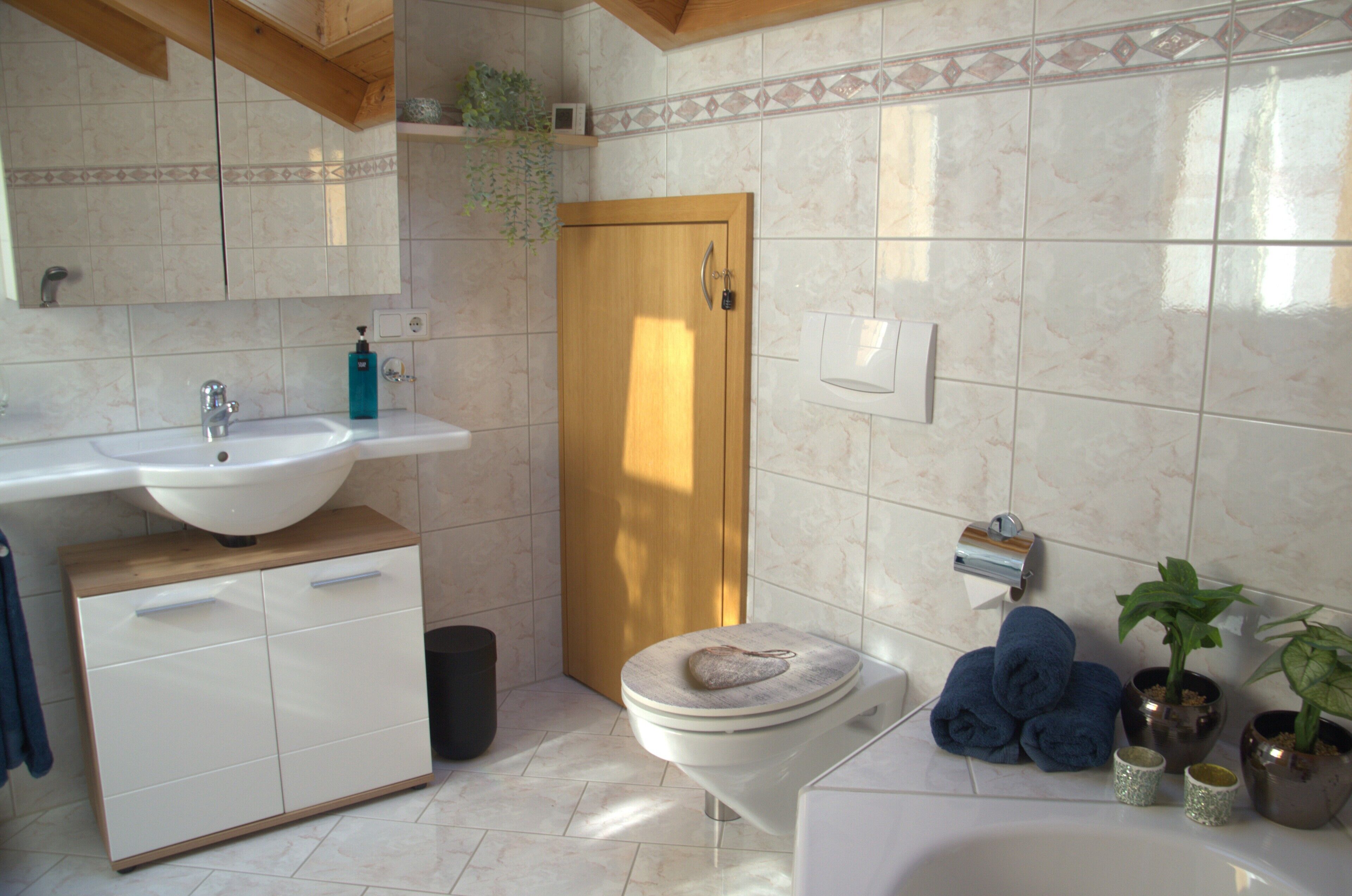 Un baño con lavamanos, inodoro y bañera. Hay toallas y plantas a un lado.
