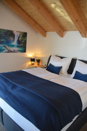 Ein Schlafzimmer mit einem Bett, Kissen, einem Nachttisch, einer Lampe und einem Wandbild.