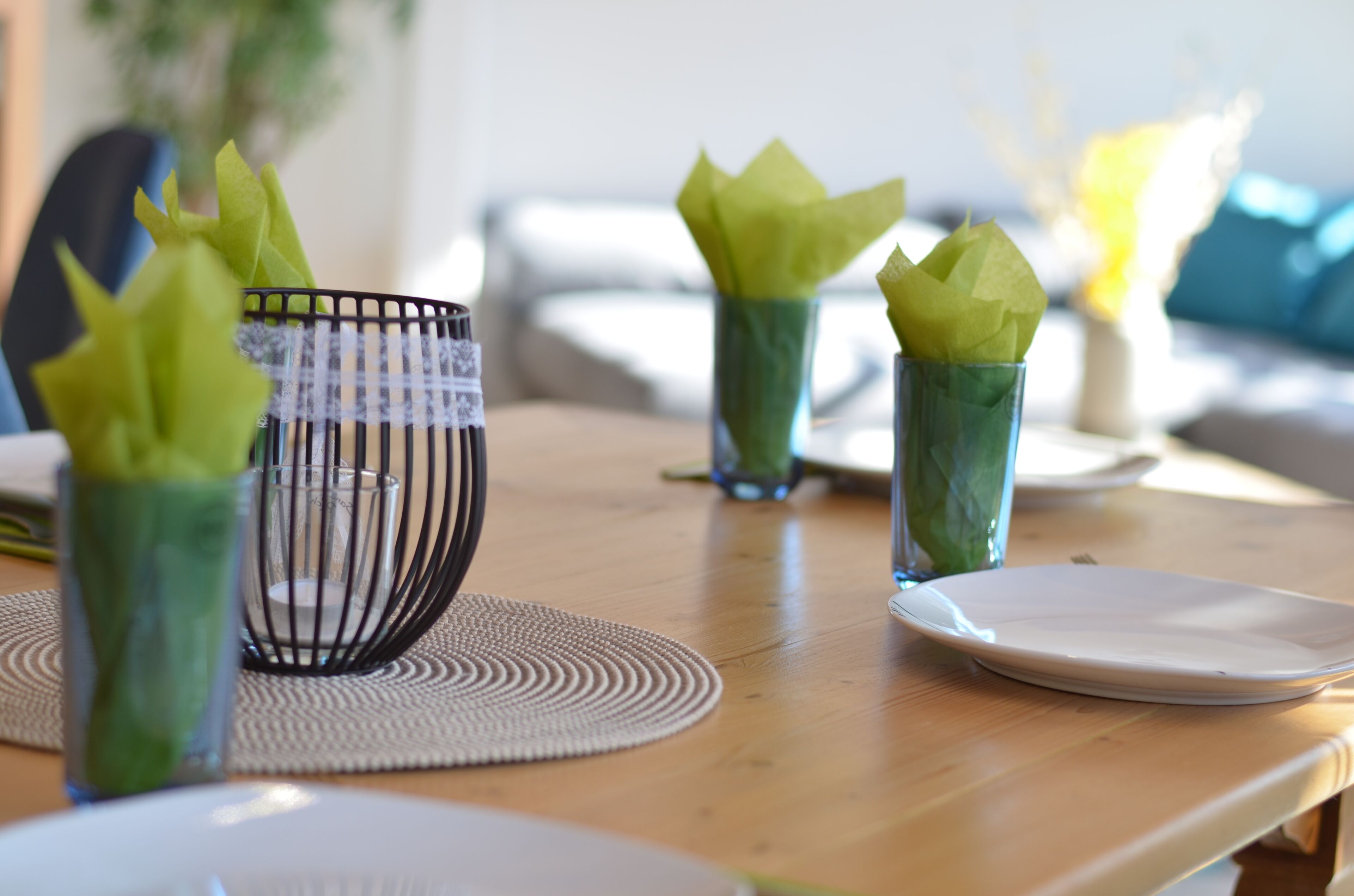 A dining table with a placemat, a glass bowl, and three glass cups with green napkins.