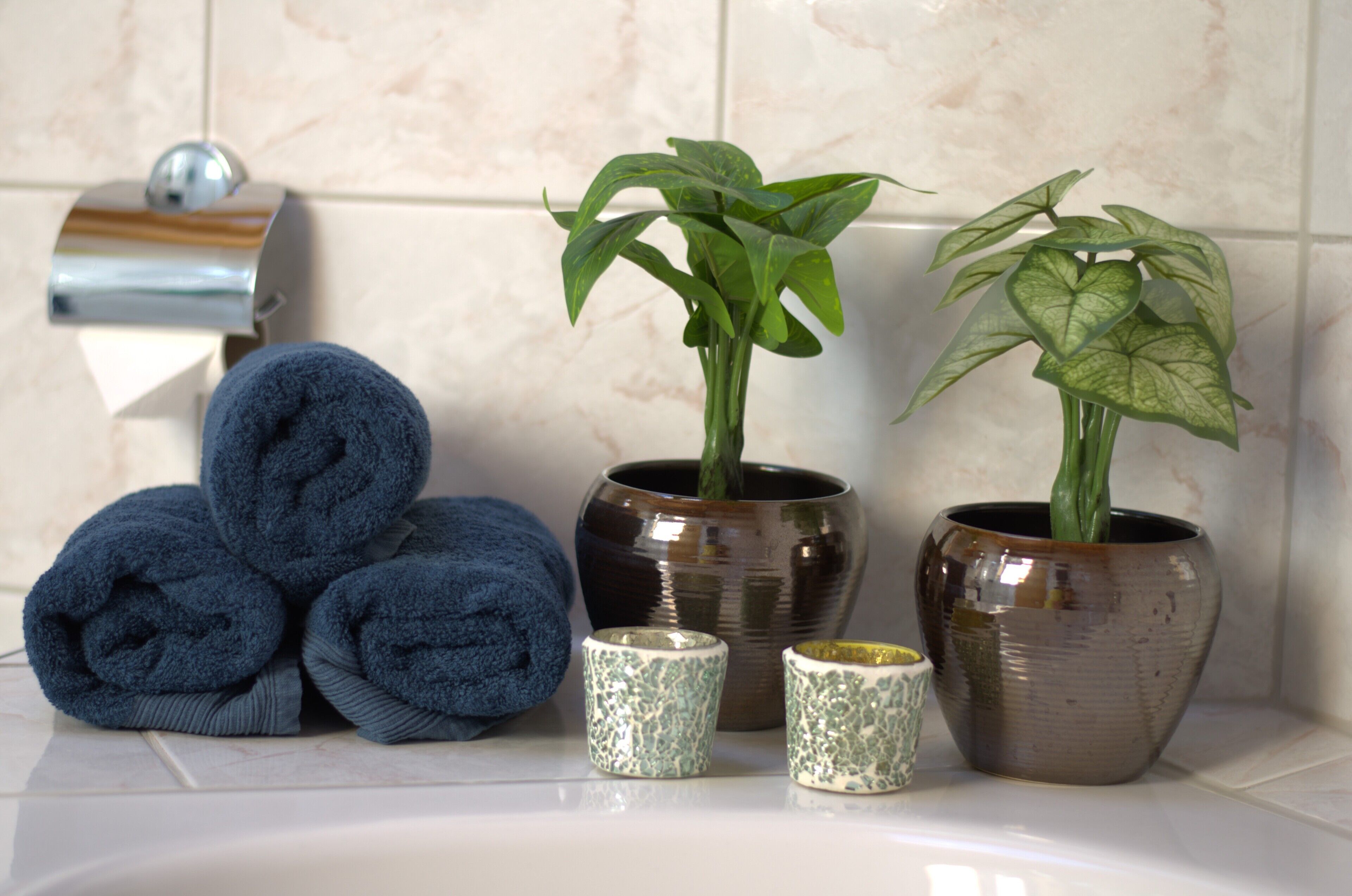 A bathroom with a towel rack, two potted plants, and a stack of towels.