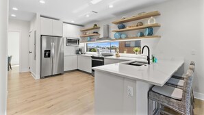 A modern kitchen with white cabinetry, stainless steel appliances, and wooden shelves above the counter.