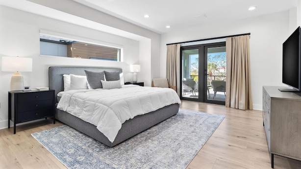 A modern bedroom with a large bed, a nightstand, a TV, and a balcony with curtains.