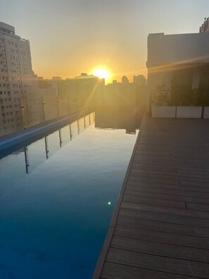 Una piscina en la azotea con vistas despejadas al atardecer y al horizonte de la ciudad.