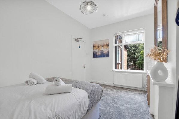 Relax in a serene bedroom with a neatly made bed, large window, and greenery view.