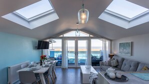 A modern interior with a dining area, a sofa, and a view of the sea through large windows. - 3 Bed pet friendly Beach House with sea views (Westward Ho!)