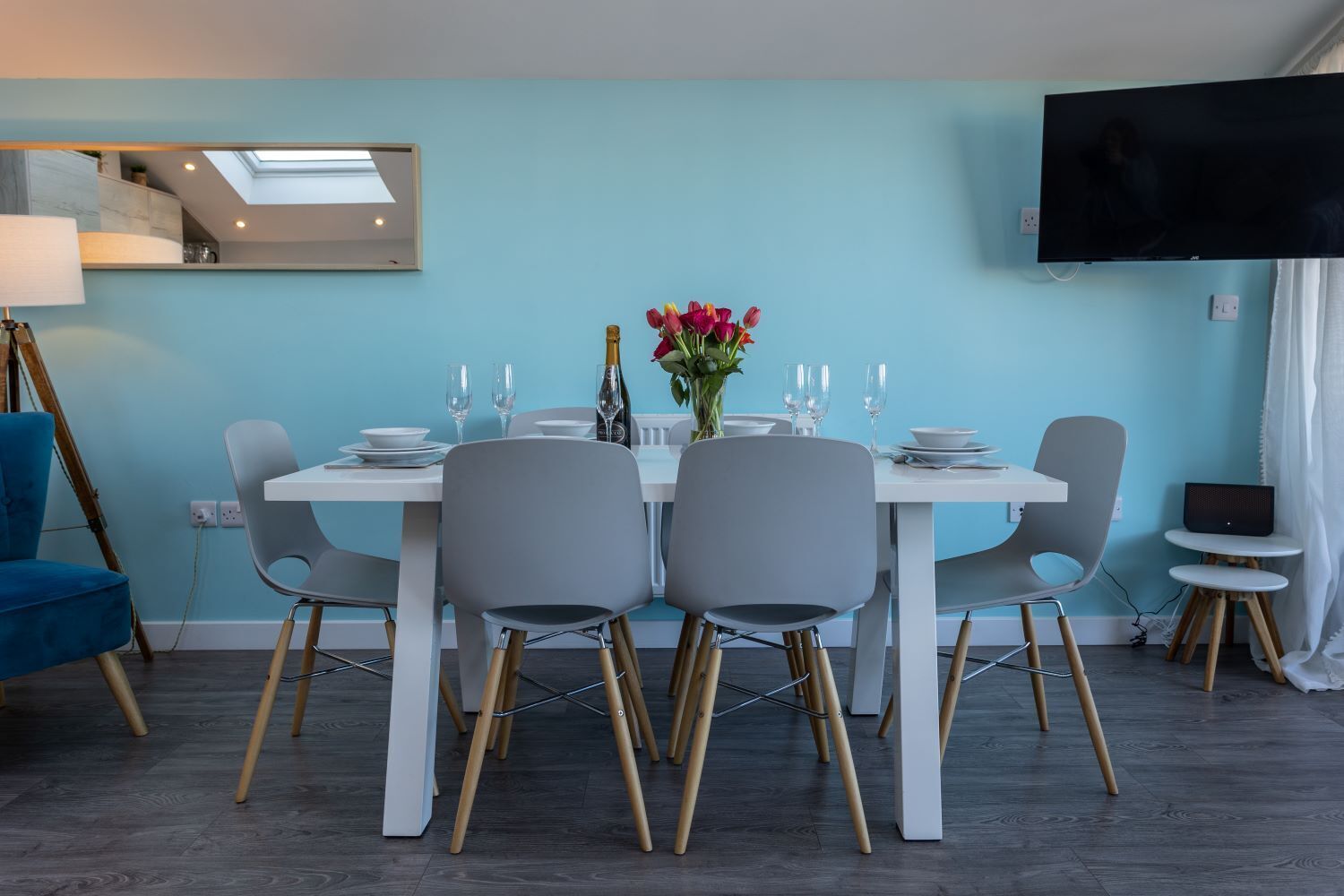 Un coin repas avec une table dressée pour quatre personnes, un vase de fleurs et un téléviseur à écran plat fixé au mur.
