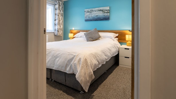 Une chambre à coucher avec un lit, des tables de chevet, un tableau et une fenêtre avec des rideaux.