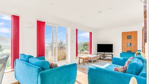 En rummelig stue med stort fjernsyn, blå sofaer og en skydedør til en have.