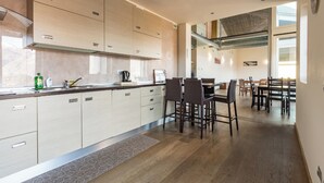 A modern kitchen with light wood cabinets, a central island, and a dining area with dark chairs. - Villa Corvina by My Villa Collection (Tremezzo)