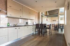 A modern kitchen with light wood cabinets, a central island, and a dining area with dark chairs. - Villa Corvina by My Villa Collection (Tremezzo)
