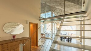 A modern interior with a wooden cabinet, a round mirror, and a staircase leading to an upper level with glass railings and a view of the outdoors. - Villa Corvina by My Villa Collection (Tremezzo)