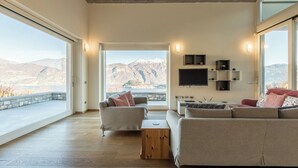 A spacious living room with a large window offering a mountain view, a flat-screen TV mounted on the wall, and a cozy seating area with a sofa and armchairs. - Villa Corvina by My Villa Collection (Tremezzo)