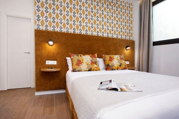 A hotel room with a wooden headboard, two bedside tables, a bed with floral-patterned pillows, and a magazine on the bed.
