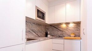 Een kleine keuken met witte kasten, een marmeren spatwand en een ingebouwde magnetron.
