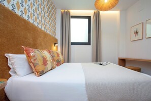 A neatly made bed with white and patterned bedding, a wooden headboard, and a bedside table with a lamp. - Genteel Home Gamazo I (Seville)
