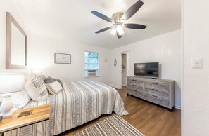 A bedroom with a bed, a dresser, a ceiling fan, a TV, and a window.