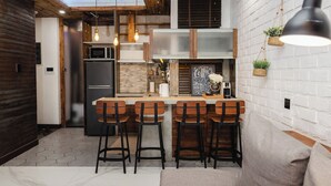 A modern kitchen with a central island, bar stools, hanging pendant lights, and a white brick wall. - Chic 1BR Retreat: Steps to Rasfannu Beach & Malé’s Best (Malé)