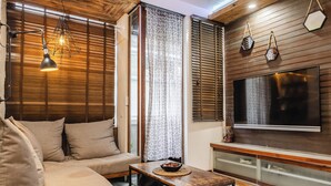 A modern living room with a sectional sofa, a coffee table with a decorative bowl, a flat-screen TV mounted on the wall, and a wooden accent wall. - Chic 1BR Retreat: Steps to Rasfannu Beach & Malé’s Best (Malé)
