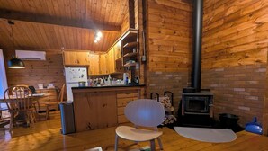 Un acogedor interior de cabaña con paredes y suelos de madera, una zona de cocina con estufa y un comedor con sillas y mesa.