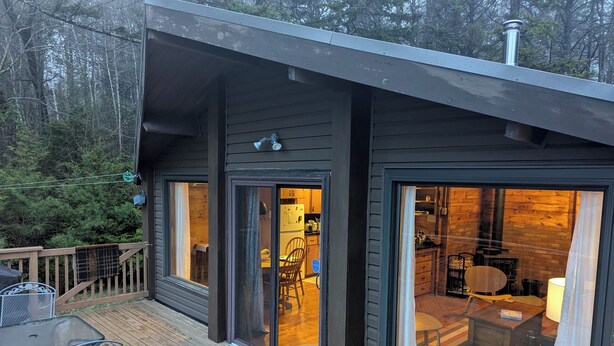 Una cabaña moderna con amplios ventanales, una terraza y un interior visible con chimenea.
