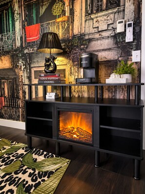 A modern living room with a fireplace, books, a coffee maker, and a decorative lamp. - Romantic  Couples Getaway • W/Fireplace &Private Patio • Walk Everywhere (Saugatuck)