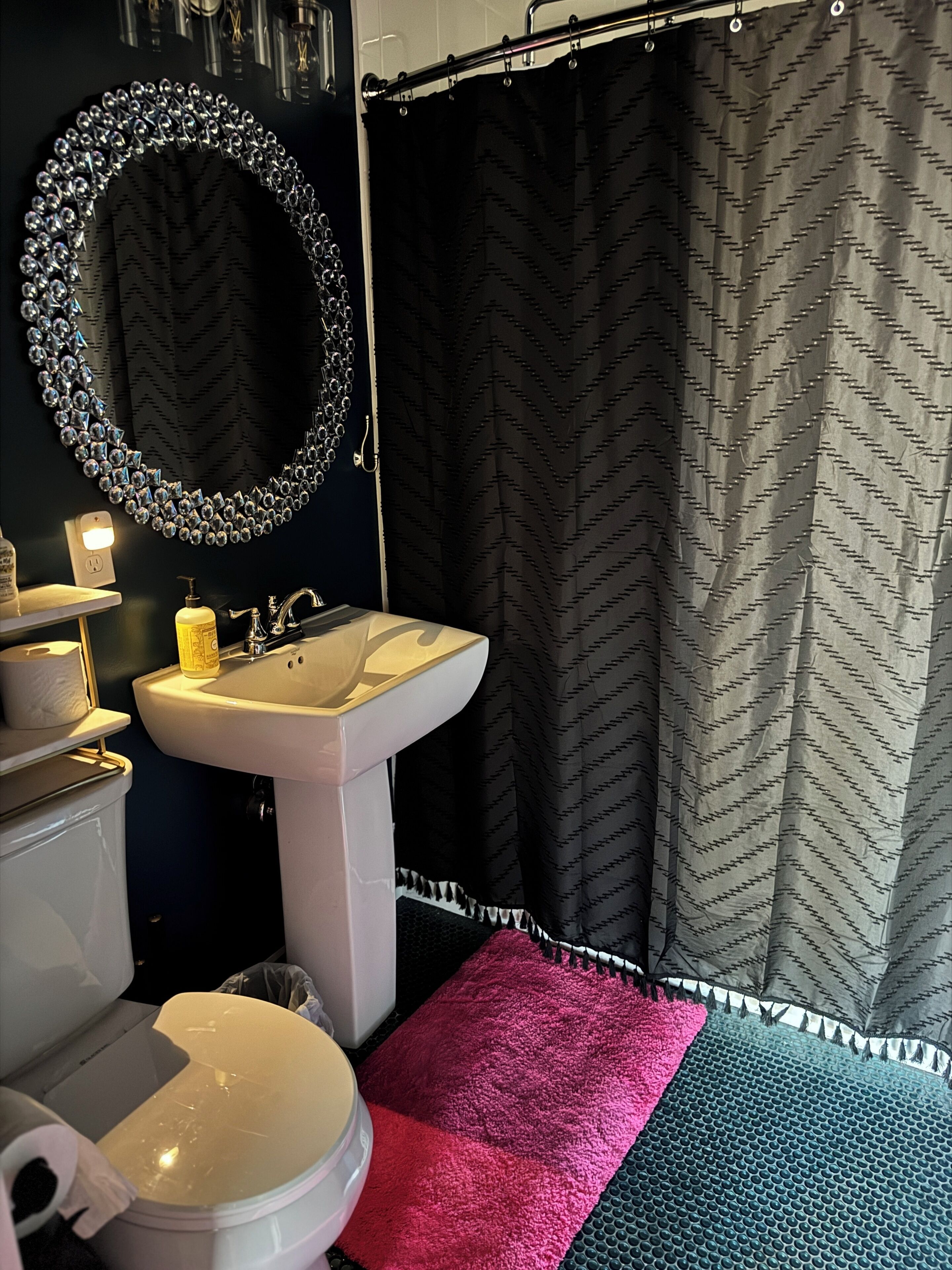 Ein Badezimmer mit einem weißen Waschbecken, einem Spiegel mit dekorativem Rahmen, einer Toilette und einer Duschvorhang mit Zickzackmuster.