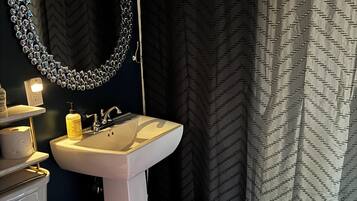 Ein Badezimmer mit einem weißen Waschbecken, einem Spiegel mit dekorativem Rahmen, einer Toilette und einer Duschvorhang mit Zickzackmuster.