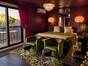 A bedroom with a large bed, two green armchairs, a chaise lounge, a leopard print rug, a chandelier, and a large window with curtains. - Romantic  Couples Getaway • W/Fireplace &Private Patio • Walk Everywhere (Saugatuck)