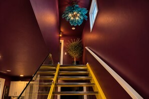 Un escalier avec une rampe jaune menant à un palier où se trouve une plante en pot et un luminaire décoratif au plafond.