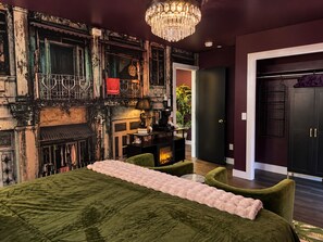 A room with a fireplace, a bed with a green bedspread, a chandelier, and a dark-colored wardrobe. - Romantic  Couples Getaway • W/Fireplace &Private Patio • Walk Everywhere (Saugatuck)