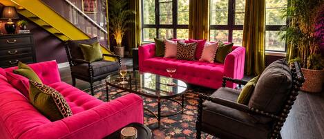 A modern living room with a staircase, a pink sofa set, and a glass coffee table.