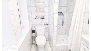 A modern bathroom with white marble tiles, a toilet, a shower, and a bathtub.