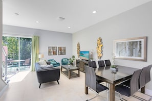 A modern living room with a dining area, large windows, and a balcony.