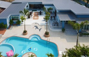 Un bâtiment moderne doté d’une piscine, d’un espace extérieur aménagé et de palmiers.