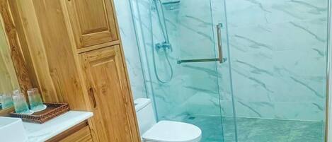 Un baño con tocador de madera, cabina de ducha de vidrio y pared con azulejos de mármol.