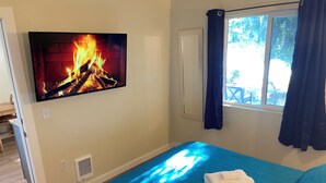 Una camera da letto con TV che mostra un camino, un letto con copriletto blu, una finestra con tende e vista sull'esterno.