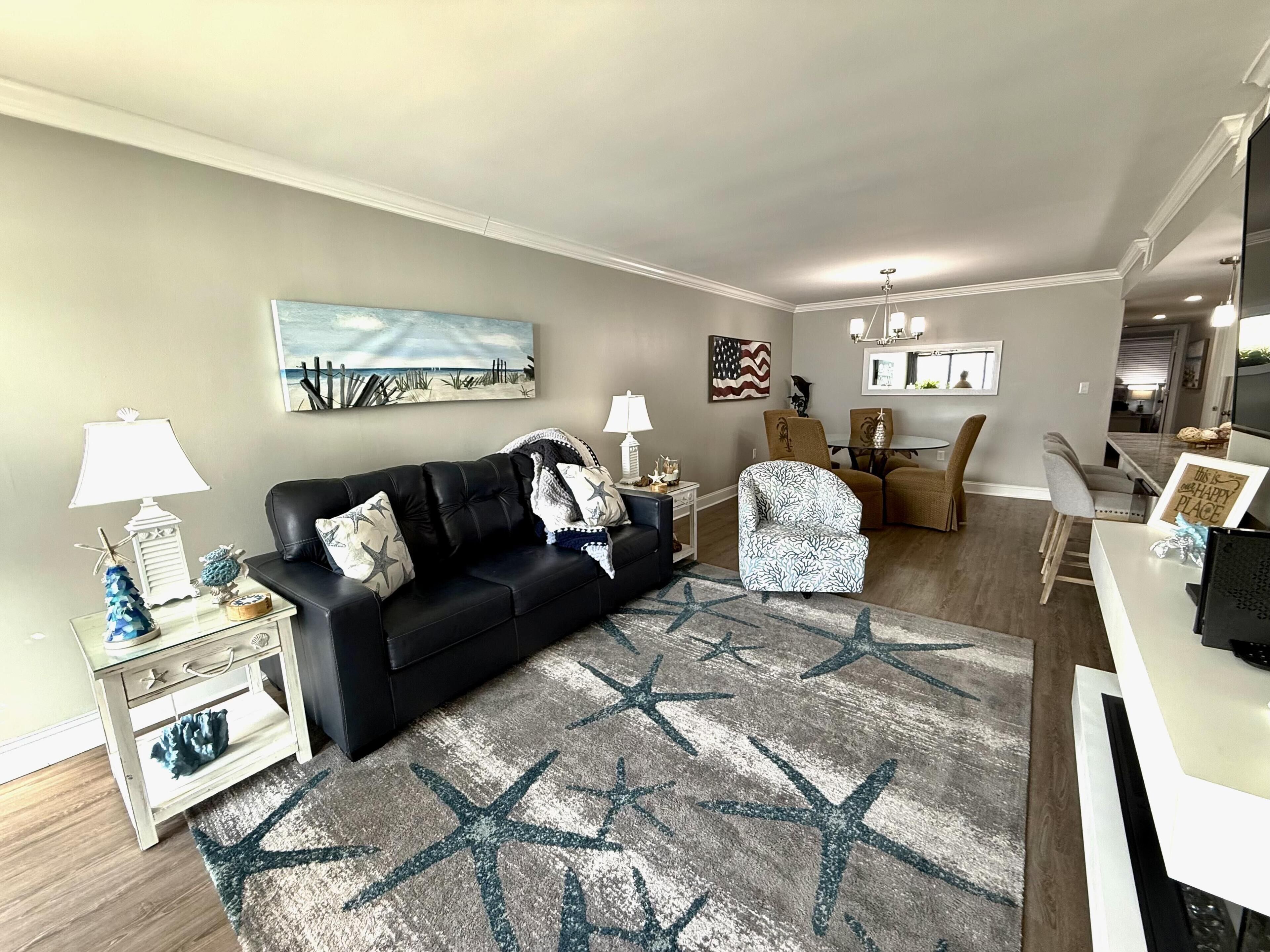 A living room with a black leather sofa, a patterned armchair, a star-patterned rug, a painting of a beach, and a framed American flag.