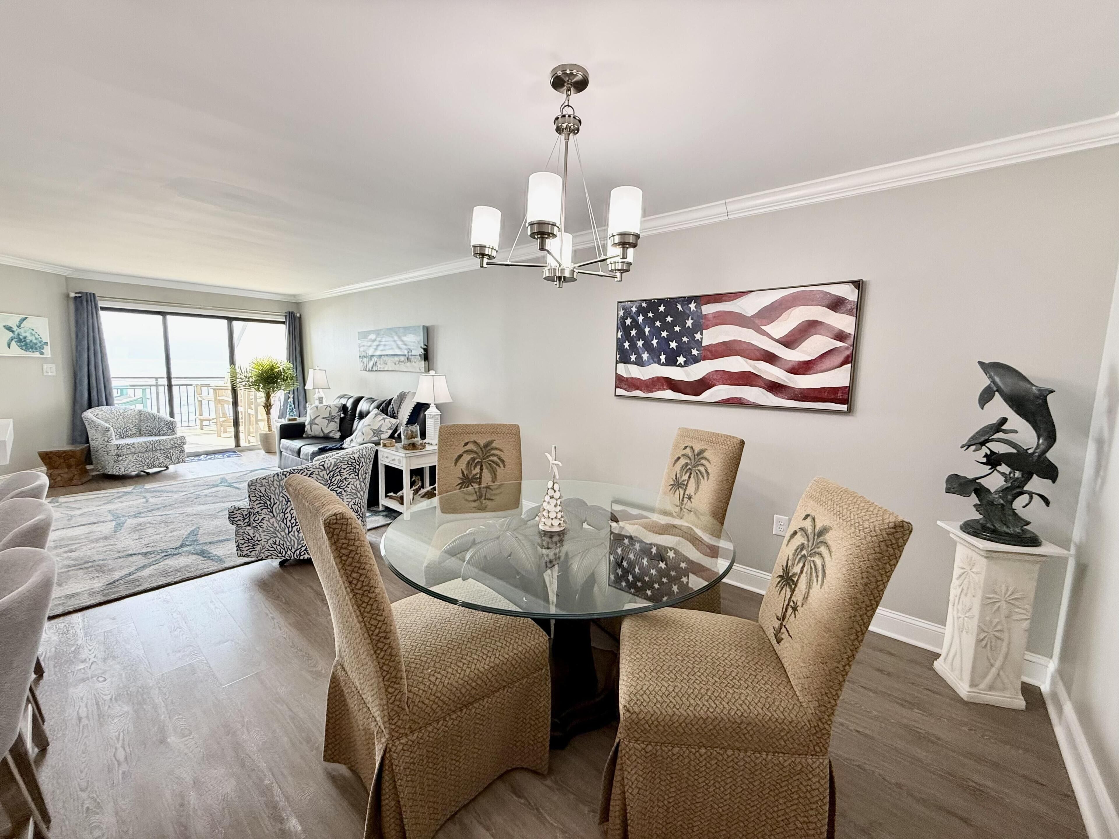 A dining area with a glass table, chairs, and a chandelier. There is a large American flag on the wall.