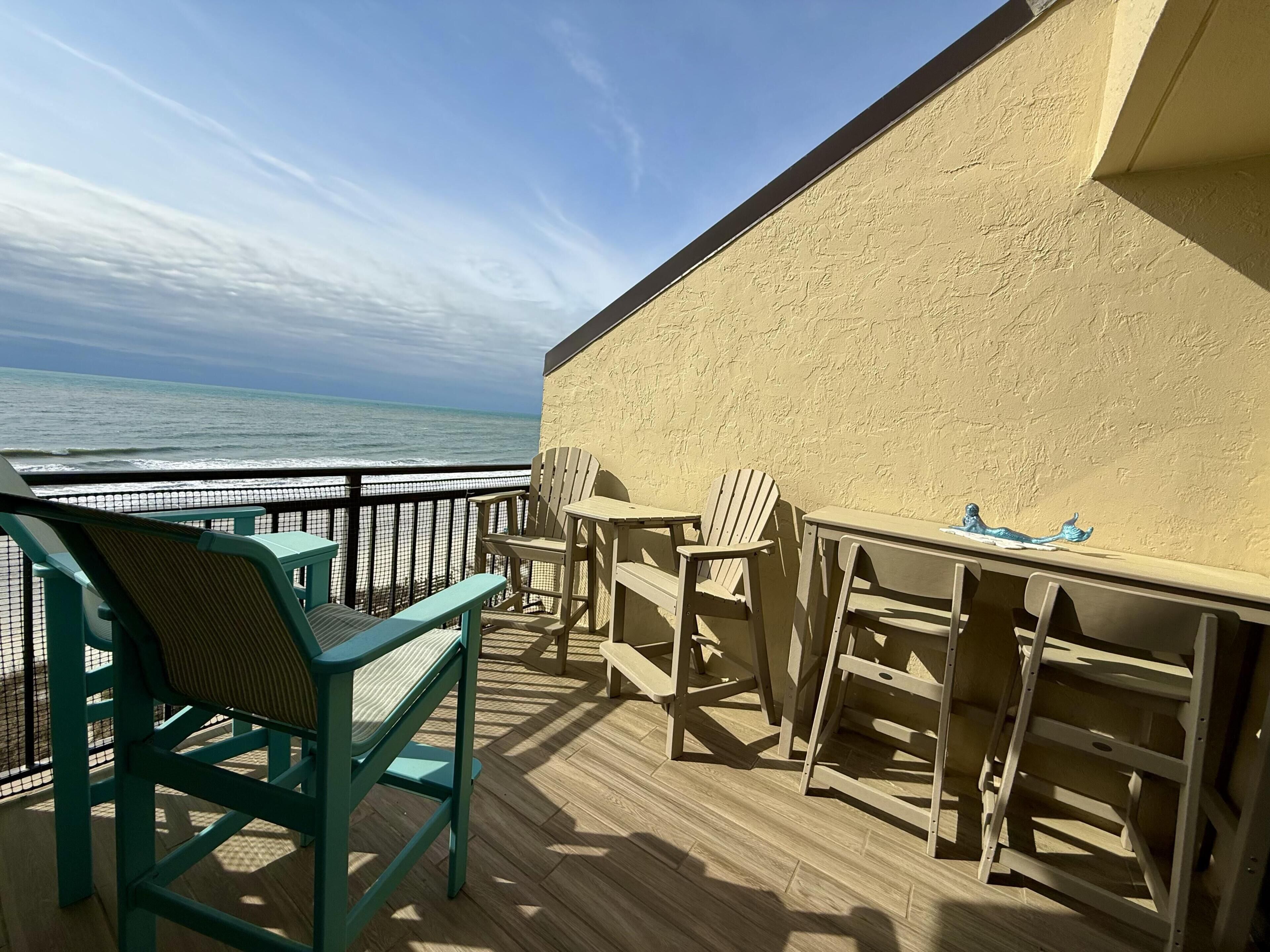 A deck with chairs and tables, overlooking the ocean.