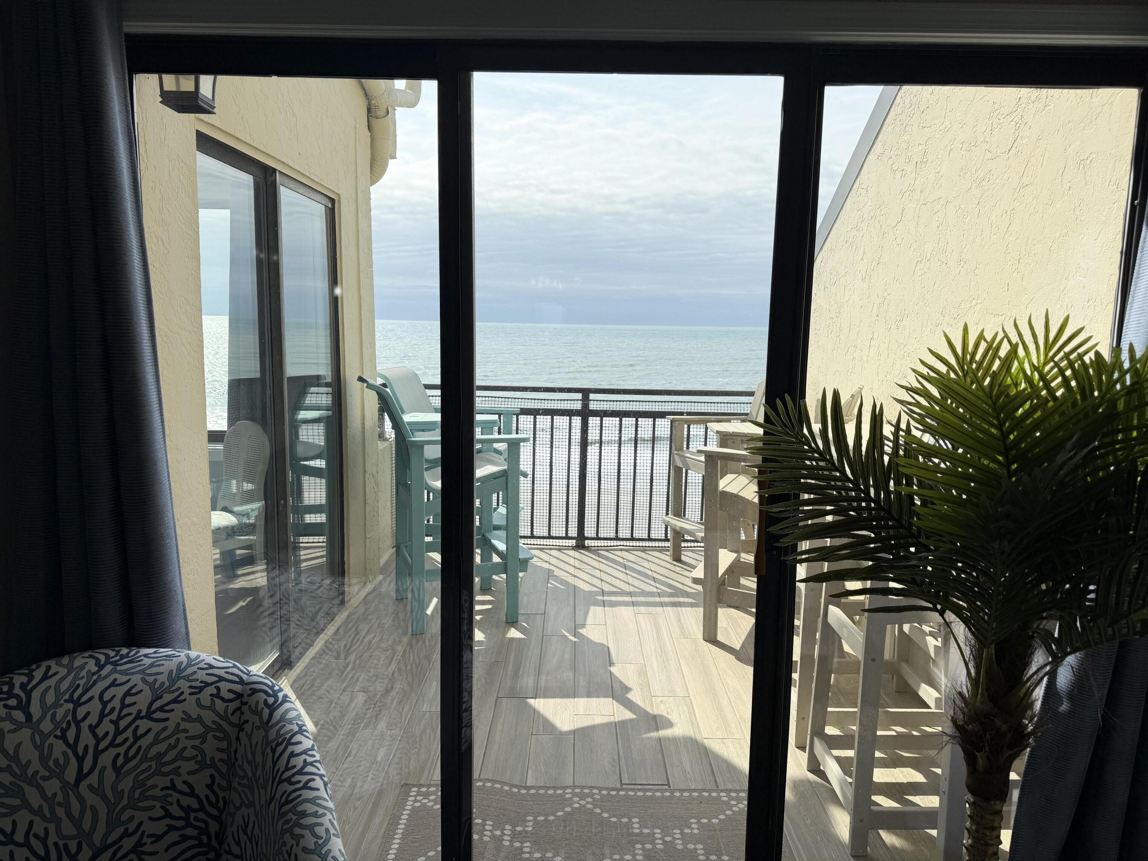 Een balkon met uitzicht op zee, een stoel, een tafel en een plant in een pot.