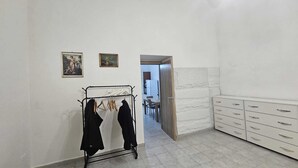 Ein Zimmer mit einem Wäscheständer aus Metall, einer weißen Kommode mit Schubladen und einer Tür zu einem Essbereich.