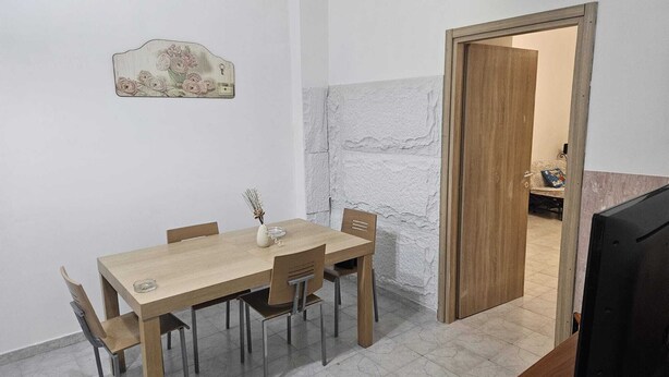 Ein Essbereich mit Holztisch und Stühlen, einer Vase mit Trockenblumen und einer strukturierten Wand.