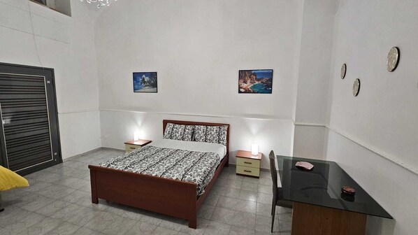A bedroom with a bed, bedside tables, a desk, and two wall-mounted pictures.