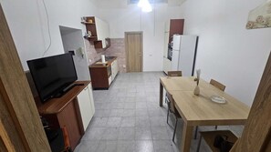 A compact kitchen with a TV, a dining table, and a refrigerator.